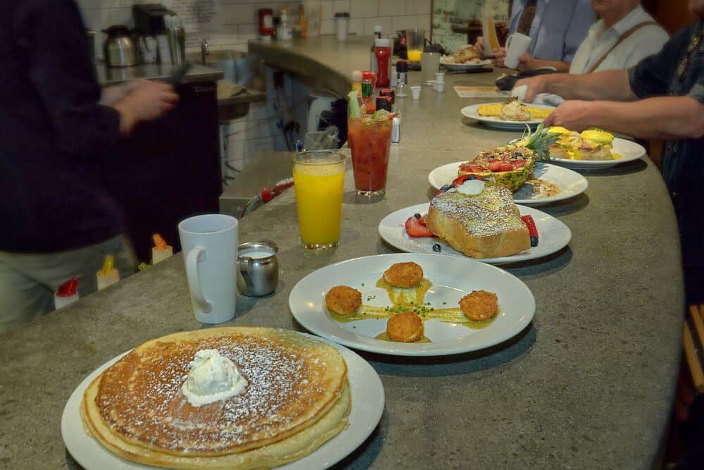 pancakes, french toast, and other breakfast food on plates at bar